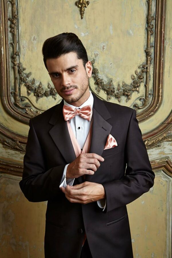 A man poses in front of an elaborately decorated wall, he is wearing the Chocolate Tuscany Tuxedo.